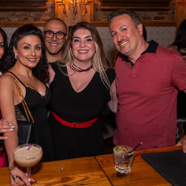 Four smiling guests, two men and two women, posing together at a bar with drinks.