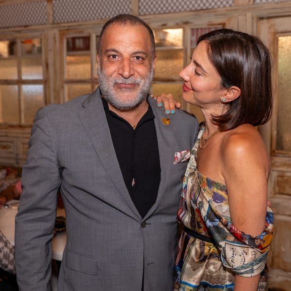 A man in a grey suit and a woman in a patterned dress pose together at Darvish Kitchen.