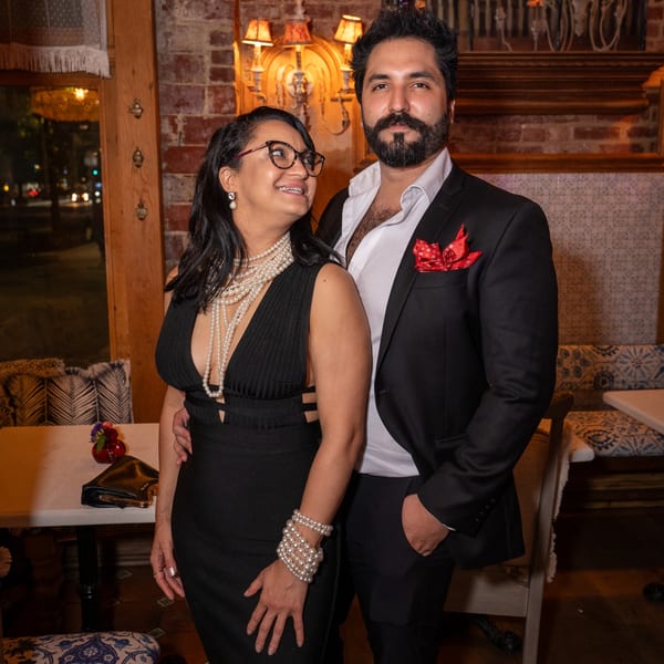 A couple dressed in formal attire posing inside Darvish Kitchen, with brick walls and ornate lighting.