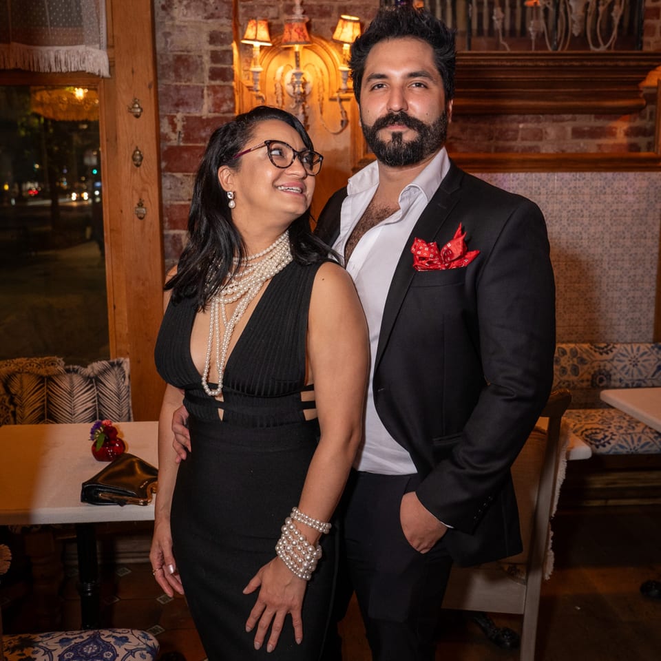 A couple dressed in formal attire posing inside Darvish Kitchen, with brick walls and ornate lighting.