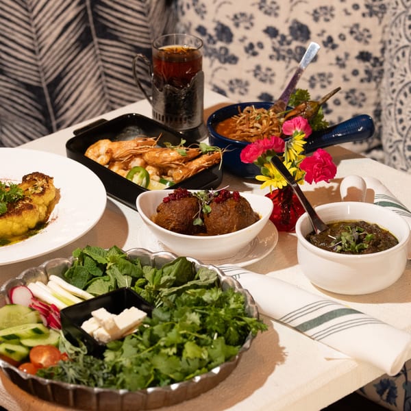 A table laden with various Persian dishes, including shrimp, meatballs, and fresh herbs.