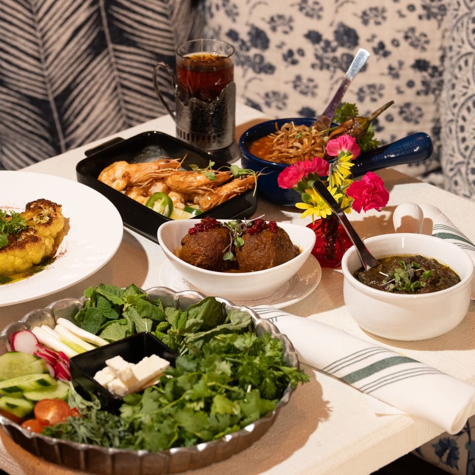 A table laden with various Persian dishes, including shrimp, meatballs, and fresh herbs.