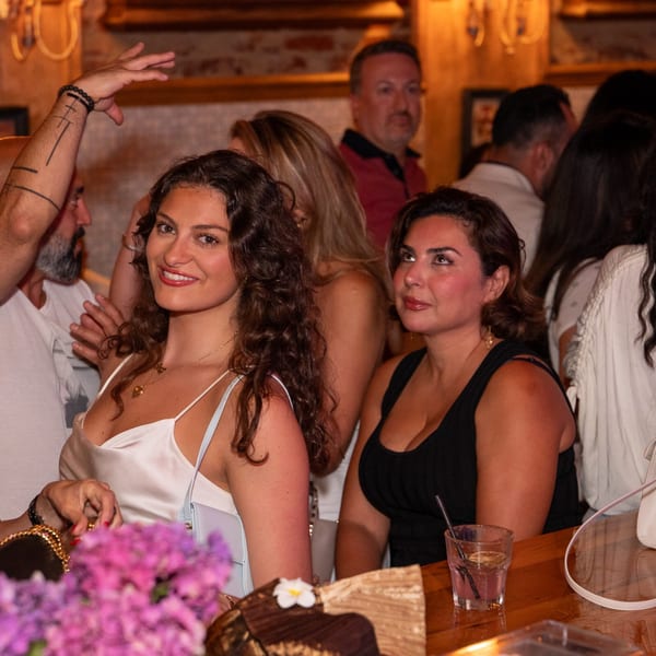 Two women smiling and looking at the camera, with other patrons in a dimly lit Darvish Kitchen.