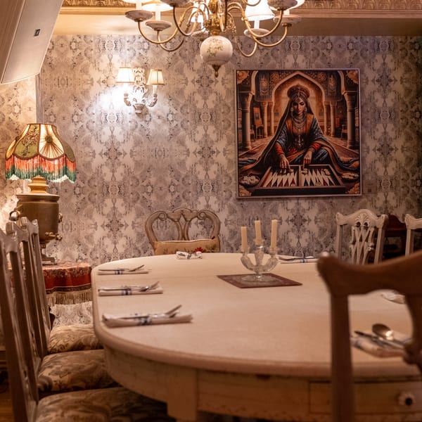Elegant dining room with patterned wallpaper, a set table, chandelier, and a painting of a woman.
