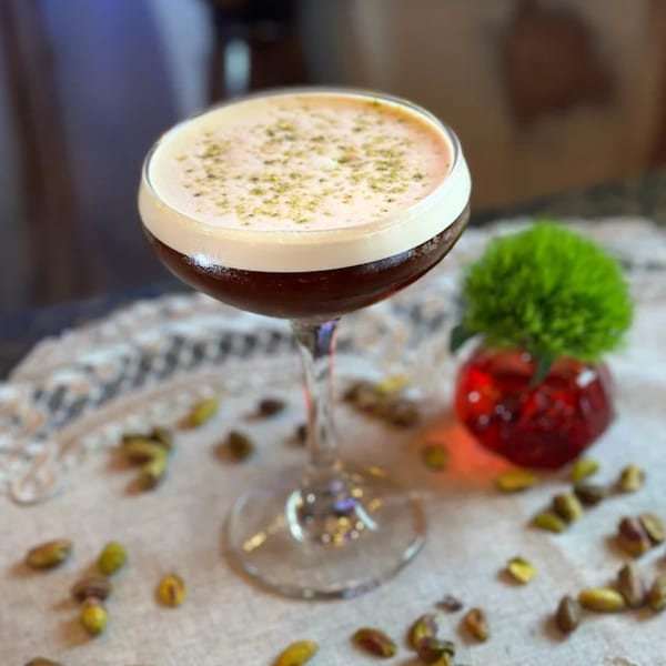 A Darvish Kitchen cocktail with foam and green garnish, surrounded by pistachios and a red decoration.