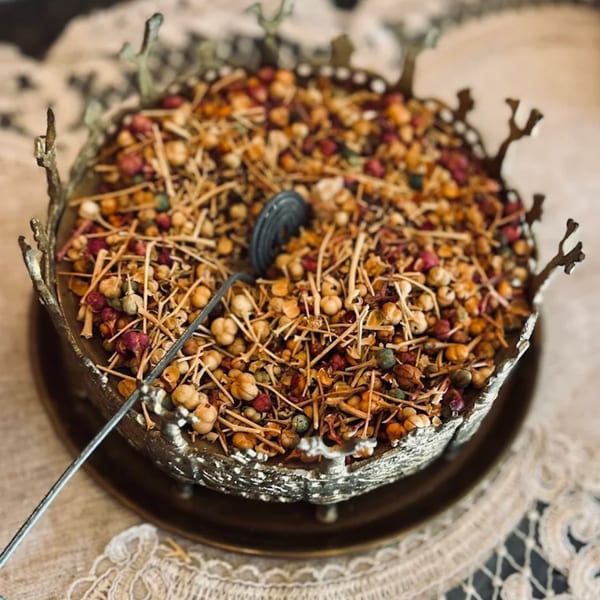 A decorative silver bowl filled with dried herbs, spices, and small red and yellow berries.