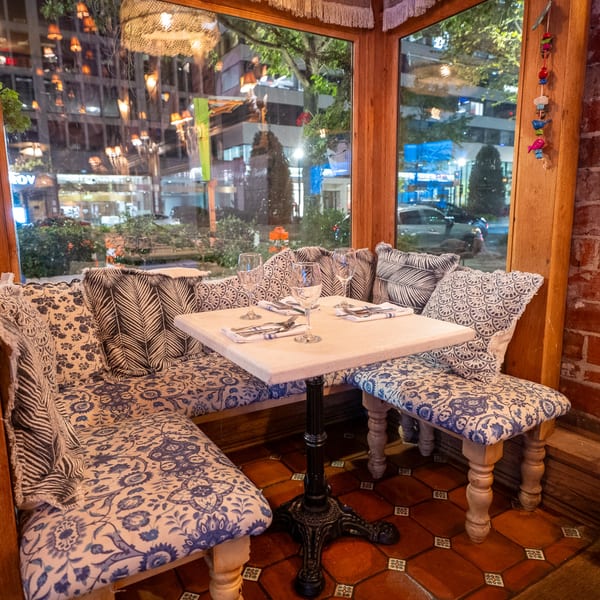Cozy corner booth with blue and white patterned cushions, set table, and large windows overlooking a city street.