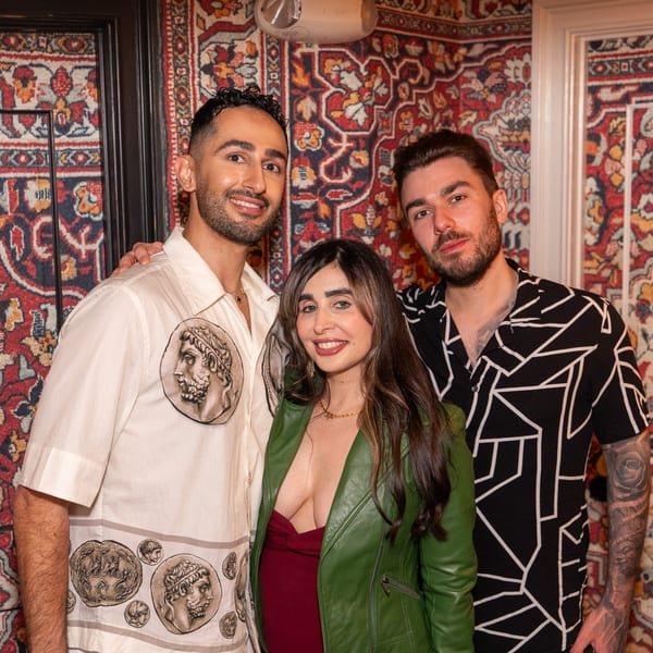 Three smiling people posing together in front of a vibrant, patterned Middle Eastern rug.