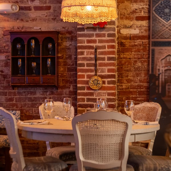 A cozy restaurant interior with a round table set with wine glasses, surrounded by elegant chairs.