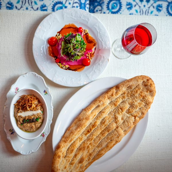 Middle-Eastern dishes: a pink beet salad, a dip with fried onions, and a large flatbread on a white tablecloth.