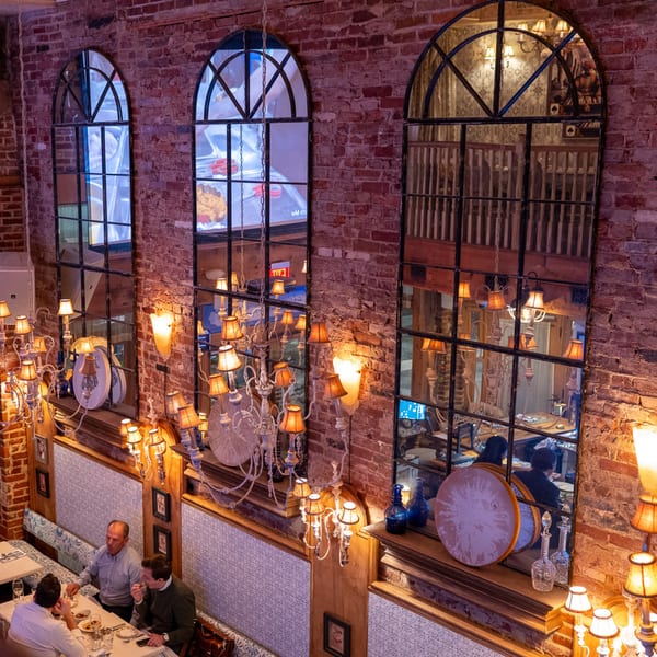 Three men dining at a restaurant table with brick walls and arched mirrors reflecting chandeliers.