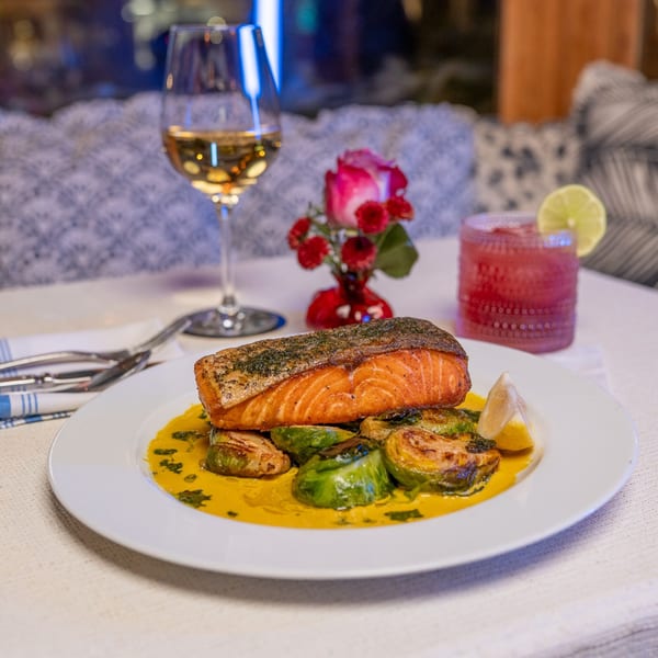 Grilled salmon with roasted brussels sprouts in a yellow sauce, white wine, and a pink cocktail.