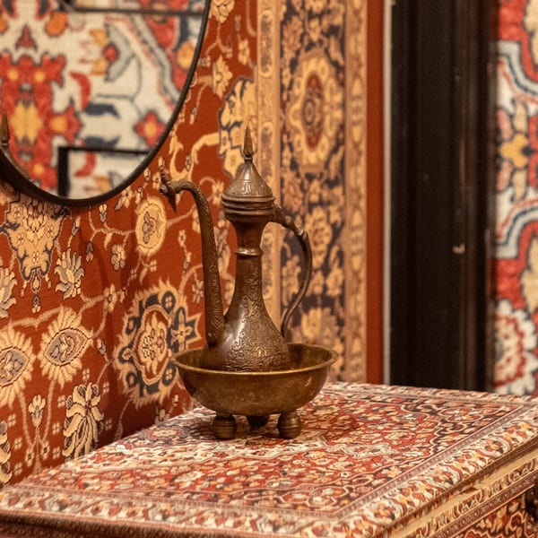 Ornate bronze pitcher and basin on a patterned rug, reflecting in a mirror, at Darvish Kitchen.
