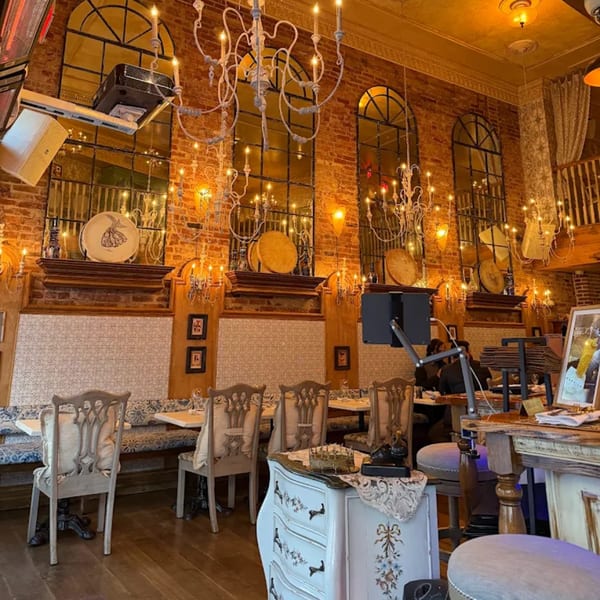 Ornate chandeliers illuminate the Darvish Kitchen dining room with brick walls and arched mirrors.