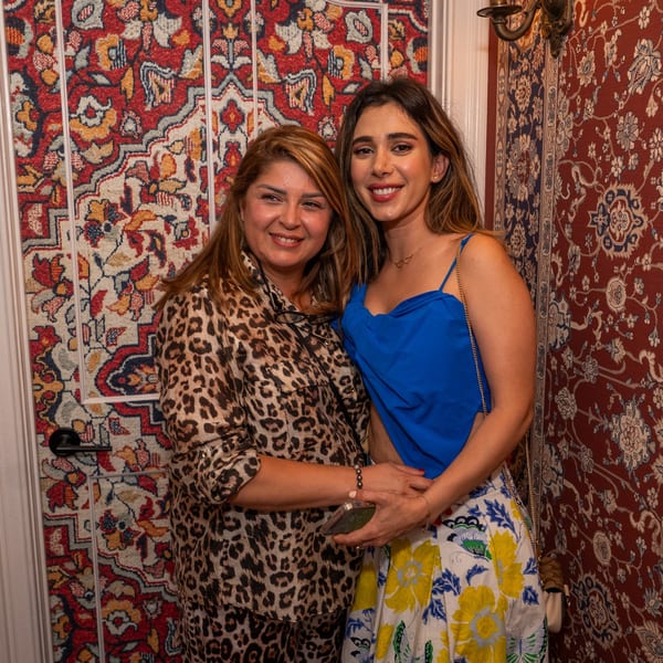 Two smiling women, one in leopard print and one in blue and floral, pose against a patterned wall.