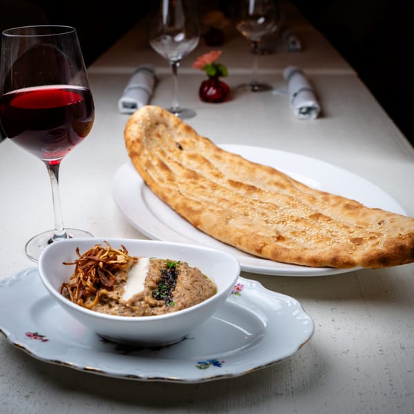 Middle-eastern appetizer with flatbread, dip topped with fried onions, and a glass of red wine.