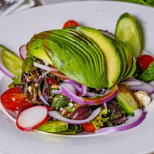 Fresh salad with sliced avocado, red onion, tomatoes, cucumbers, radishes, olives, and feta cheese.