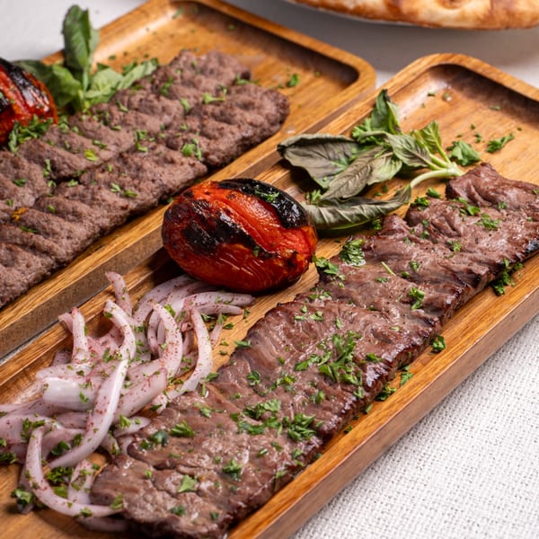Two wooden trays of Darvish Kitchen's Middle-Eastern kebabs, grilled tomatoes, onions, and fresh herbs.
